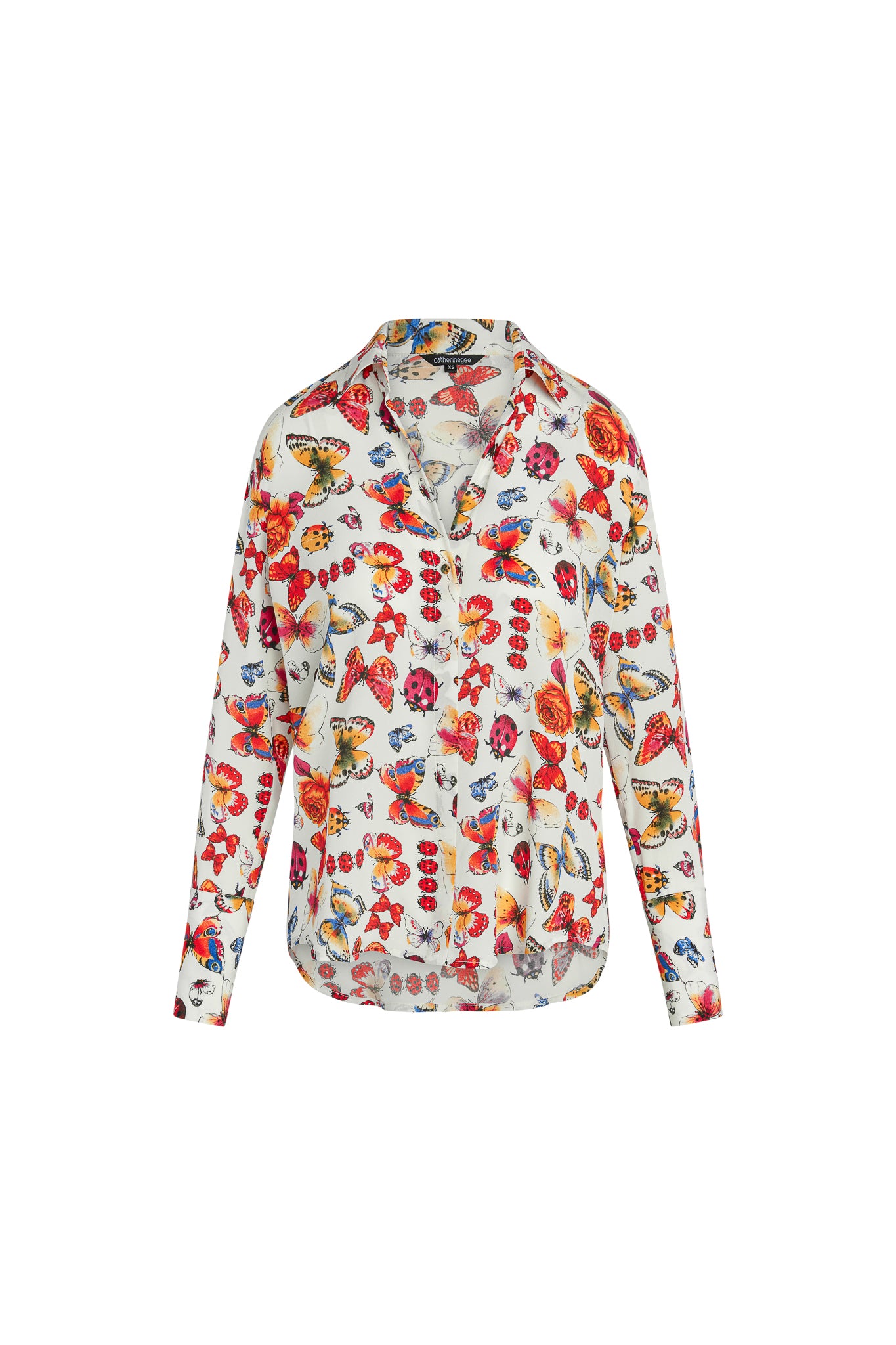 Catherine Gee Daria French Cuff Silk Blouse Ladybug. A white silk blouse with a colorful print featuring butterflies and ladybugs. The blouse has a V-neckline, long sleeves with French cuffs, and a slightly curved hem. The vibrant pattern and luxurious fabric make it a standout piece for any wardrobe.