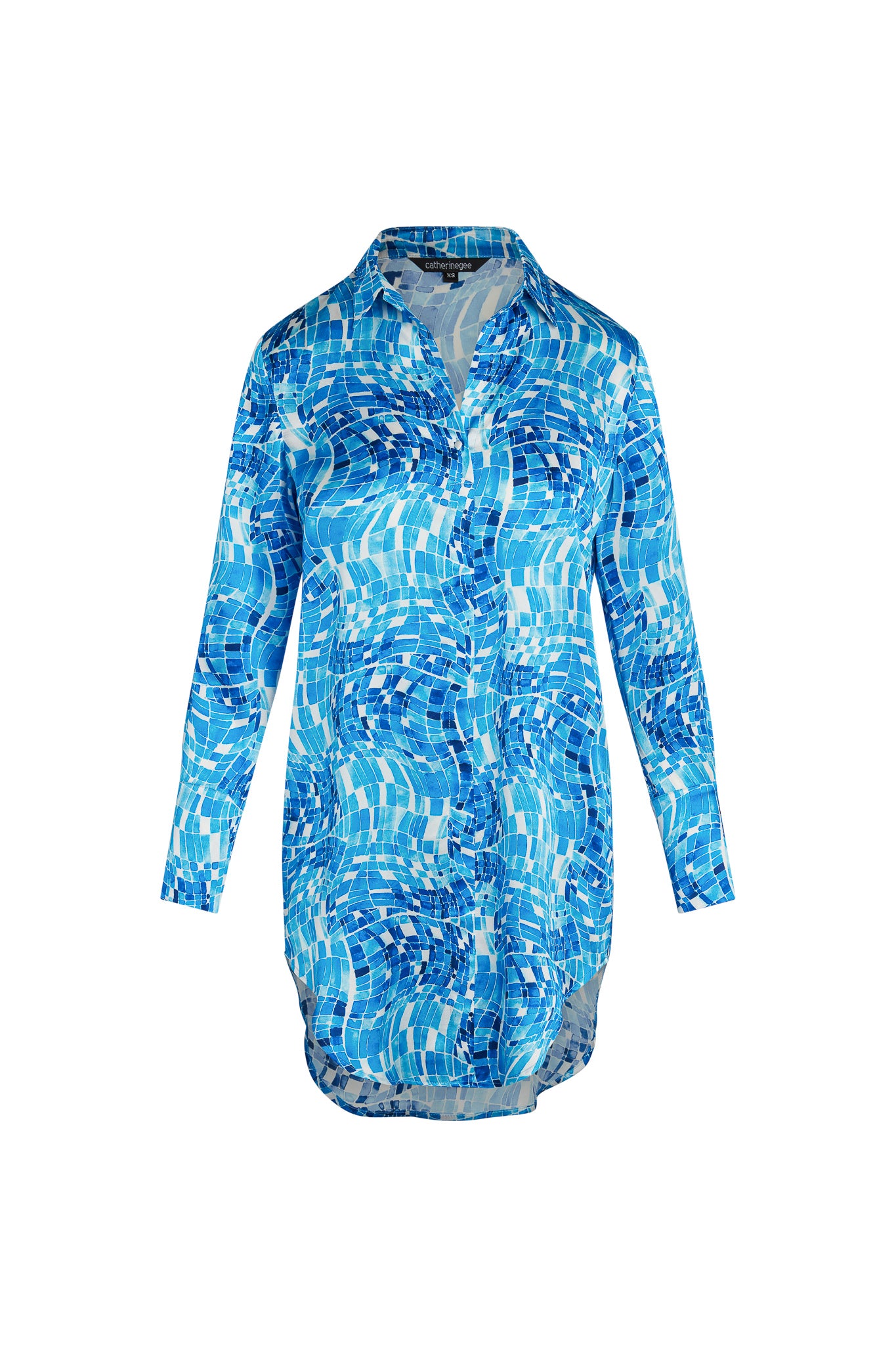 Catherine Gee Daria Shirt Pool Mosaic dress features a vibrant blue mosaic pattern reminiscent of a swimming pool, with various shades of blue and white creating a dynamic, water-like effect. The dress has a button-down front, a collar, and long sleeves, giving it a stylish and versatile look suitable for various occasions. The unique pattern and design make it an eye-catching and fashionable piece.