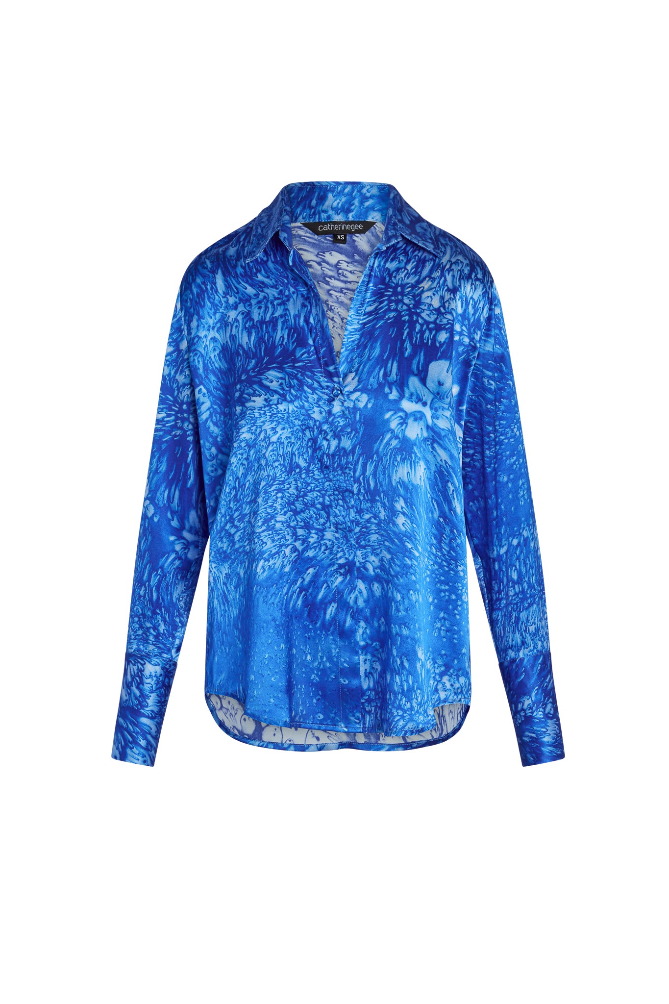 Catherine Gee Daria French Cuff Silk-Blue Dye blouse features a vibrant blue dye pattern with long sleeves, a collar, and a V-neckline. The fabric has a silky texture, and the design includes French cuffs
