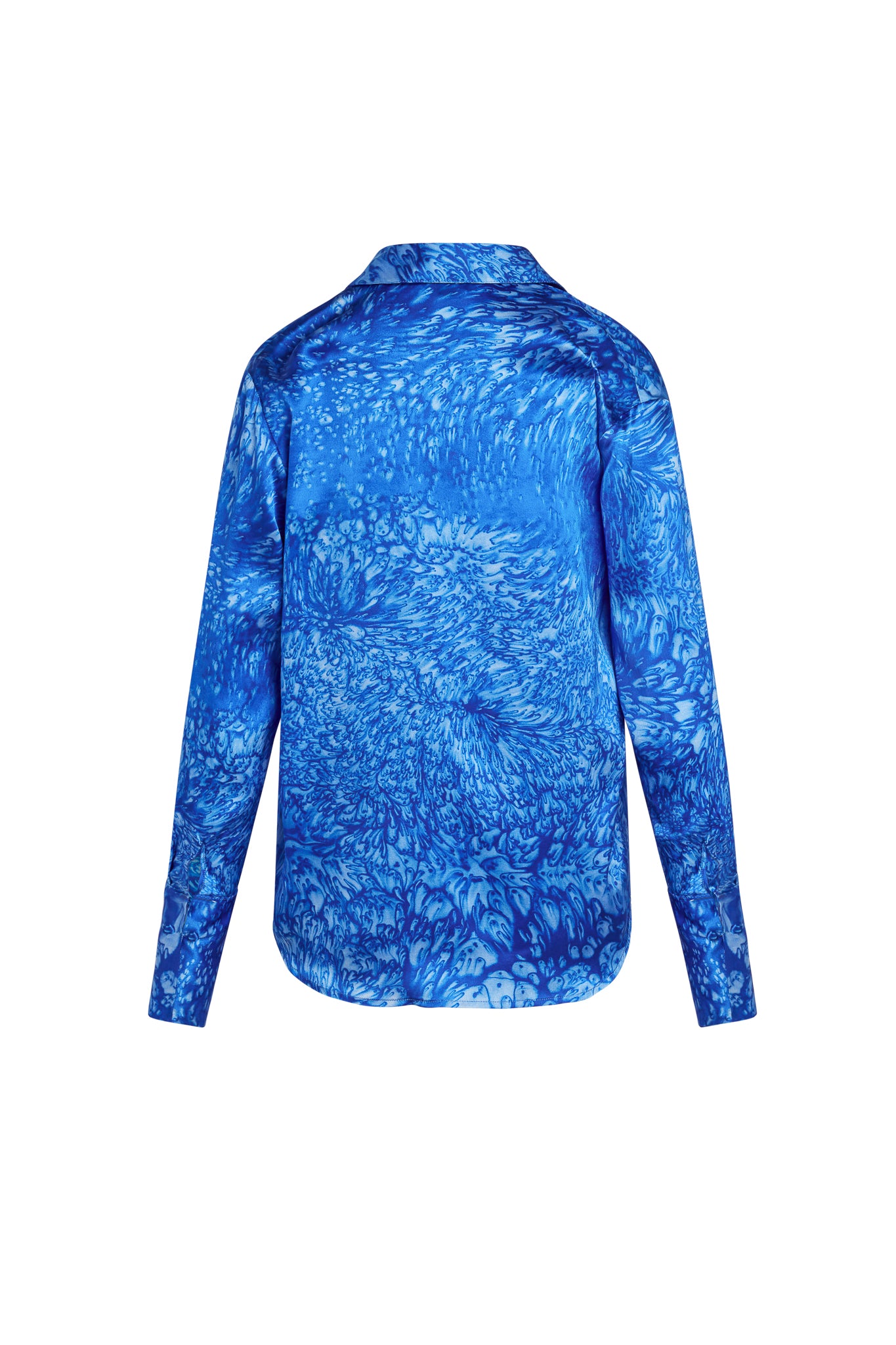 The Backview of a Catherine Gee Daria French Cuff Silk Blue Dye blouse features a vibrant blue dye pattern with long sleeves and a classic collar. The fabric has a smooth, silky texture with a slightly curved hemline.