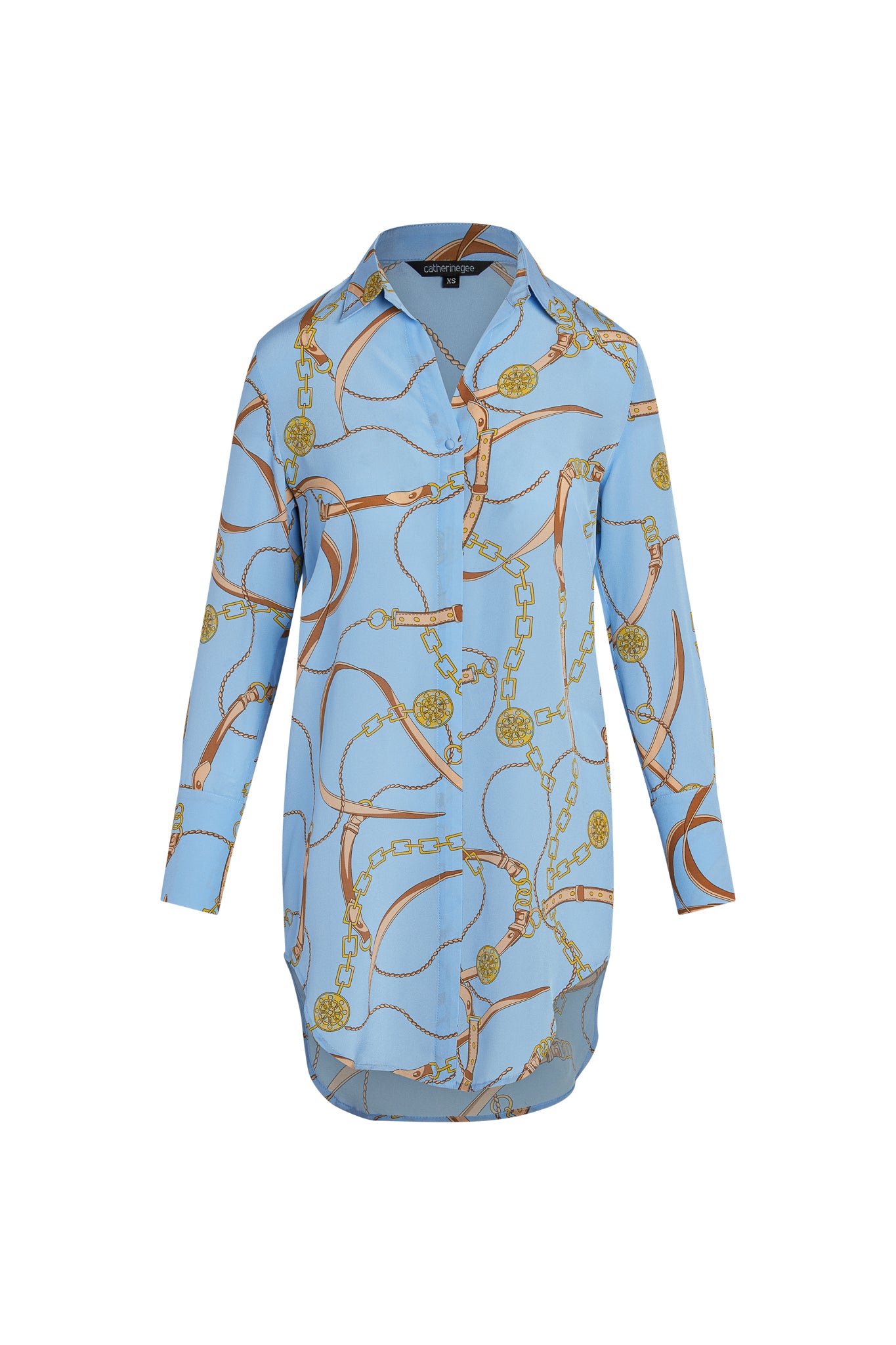 Catherine Gee Daria Shirt - San Telmo Dress. It is a long-sleeved, button-up shirt dress with a light blue base color that features a complex pattern of gold chains and medallions incorporated with brown leather straps. The design is elegant and sophisticated, making it a versatile piece suitable for both casual and formal occasions, and has a high-low hemline, adding a modern touch to its classic silhouette.