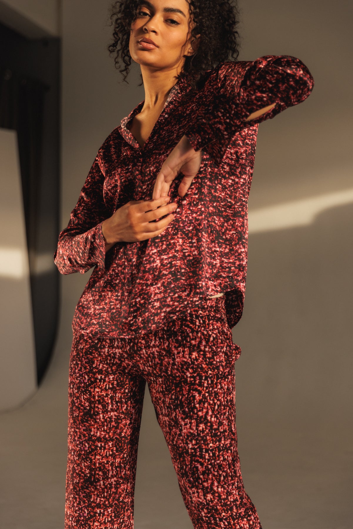 A woman wearing the Catherine Gee Daria French Cuff Silk Red Sequin Blouse, featuring a striking red and black sequin pattern. The blouse has long sleeves with French cuffs, a relaxed fit, and is paired with matching pants in the same sequin design. The shimmering fabric creates a dazzling effect, making it an eye-catching and stylish ensemble in soft natural lighting that enhances the blouse's luxurious texture and shine.