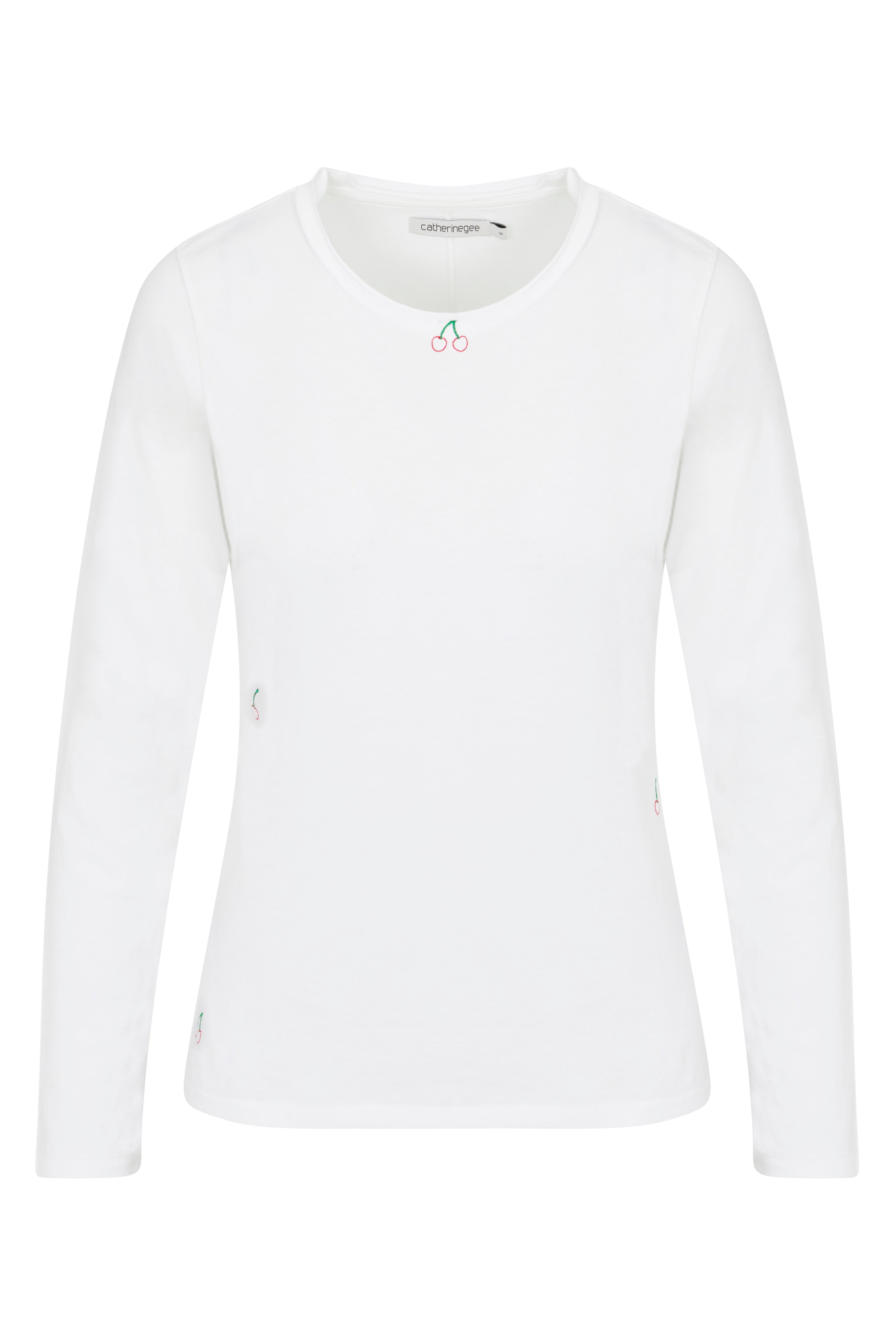 Catherine Gee Embroidered Cotton Long Sleeve Cherry T-Shirt. The shirt is white with a simple, clean design and features a small embroidered cherry motif near the neckline, adding a touch of color and charm, has a round neck and long sleeves, making it suitable for cooler weather. The minimalist design and subtle embroidery make it a versatile piece that can be dressed up or down.
