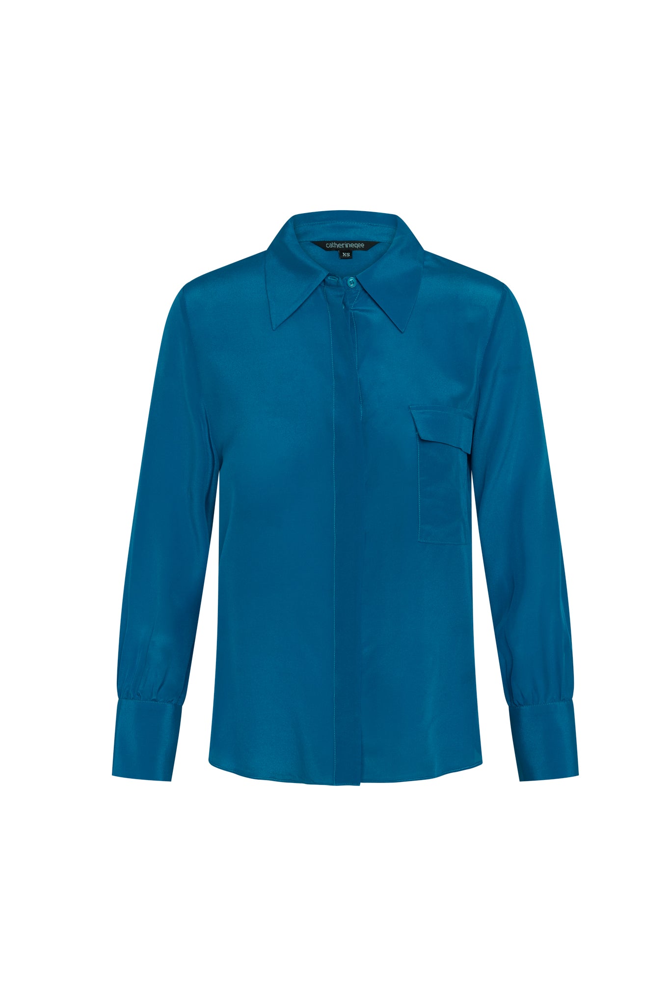 Catherine Gee Jamie True Blue Blouse. This vibrant blue blouse has a silky texture, a classic collar, and long sleeves with buttoned cuffs. It features a concealed button placket down the front and a single chest pocket on the left side. The sleek design and rich color make it a versatile piece suitable for both professional and casual settings, offering a stylish and polished look.