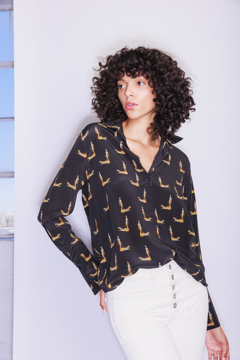 A woman wearing Catherine Gee Daria French Cuff Silk Catwoman Blouse features a straight collar, long sleeves with French cuffs, and covered buttons paired with white pants on a plain white background.