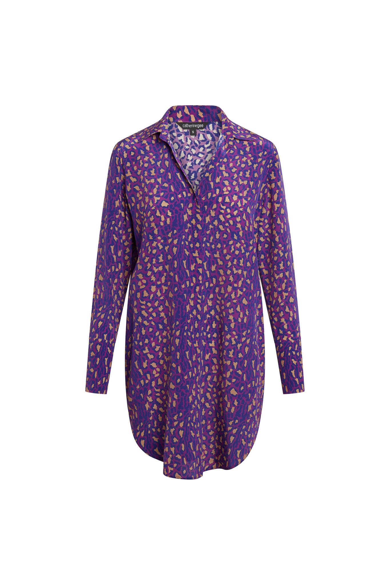Catherine Gee Daria Silk Purple Leopard Dress dress features a vibrant purple base color adorned with a leopard print pattern in contrasting shades. It has a collared neckline, long sleeves, and a slightly curved hemline, giving it a sophisticated yet playful look. The silk material adds a luxurious touch, making it suitable for both casual and formal occasions.