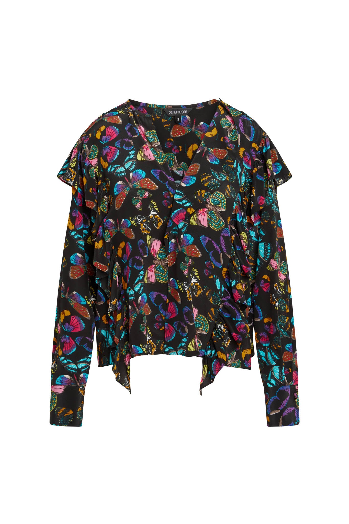 Catherine Gee Bella Blouse - The Tracy. This blouse features a vibrant, multicolored butterfly print on a black background. The design includes a V-neckline, long sleeves, and an asymmetrical hem with ruffled details, creating a stylish and dynamic look.