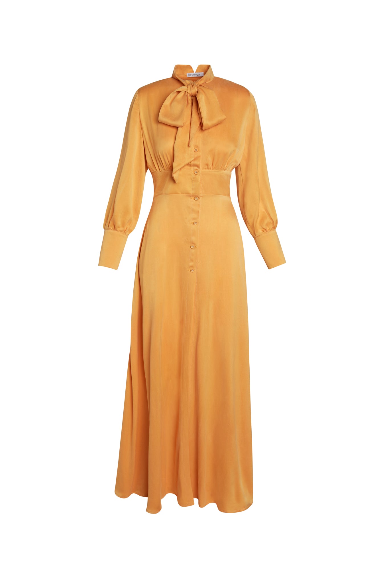Catherine Gee Electric Flou High-Slit Long dress features a vibrant Tangerine color with a silky texture. It has a high neckline adorned with a large bow tie, long sleeves with buttoned cuffs, and a fitted waist that flows into a long, flowing skirt. The front of the dress is detailed with a row of buttons running down the center, exuding a sophisticated and timeless style, making it a standout piece for formal occasions.