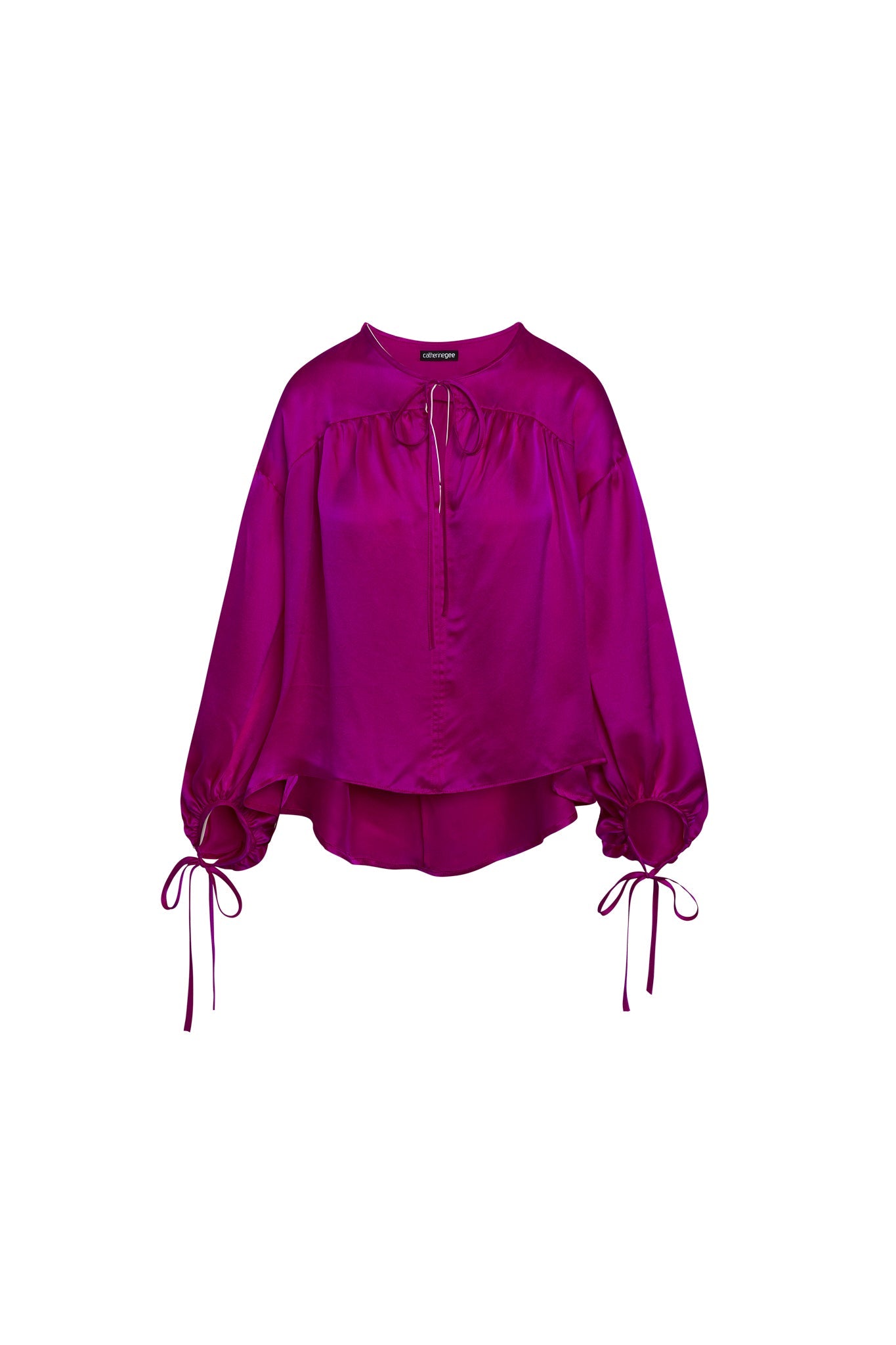 Catherine Gee Frances Hot Pink Blouse. This vibrant blouse features a loose, flowing design with long, voluminous sleeves that gather at the wrists with adjustable ties. The front has a partial button placket with a small keyhole opening at the neckline. The hemline is asymmetrical, with a slightly longer back, adding a stylish and modern touch to the garment. The rich hot pink color makes it a standout piece.