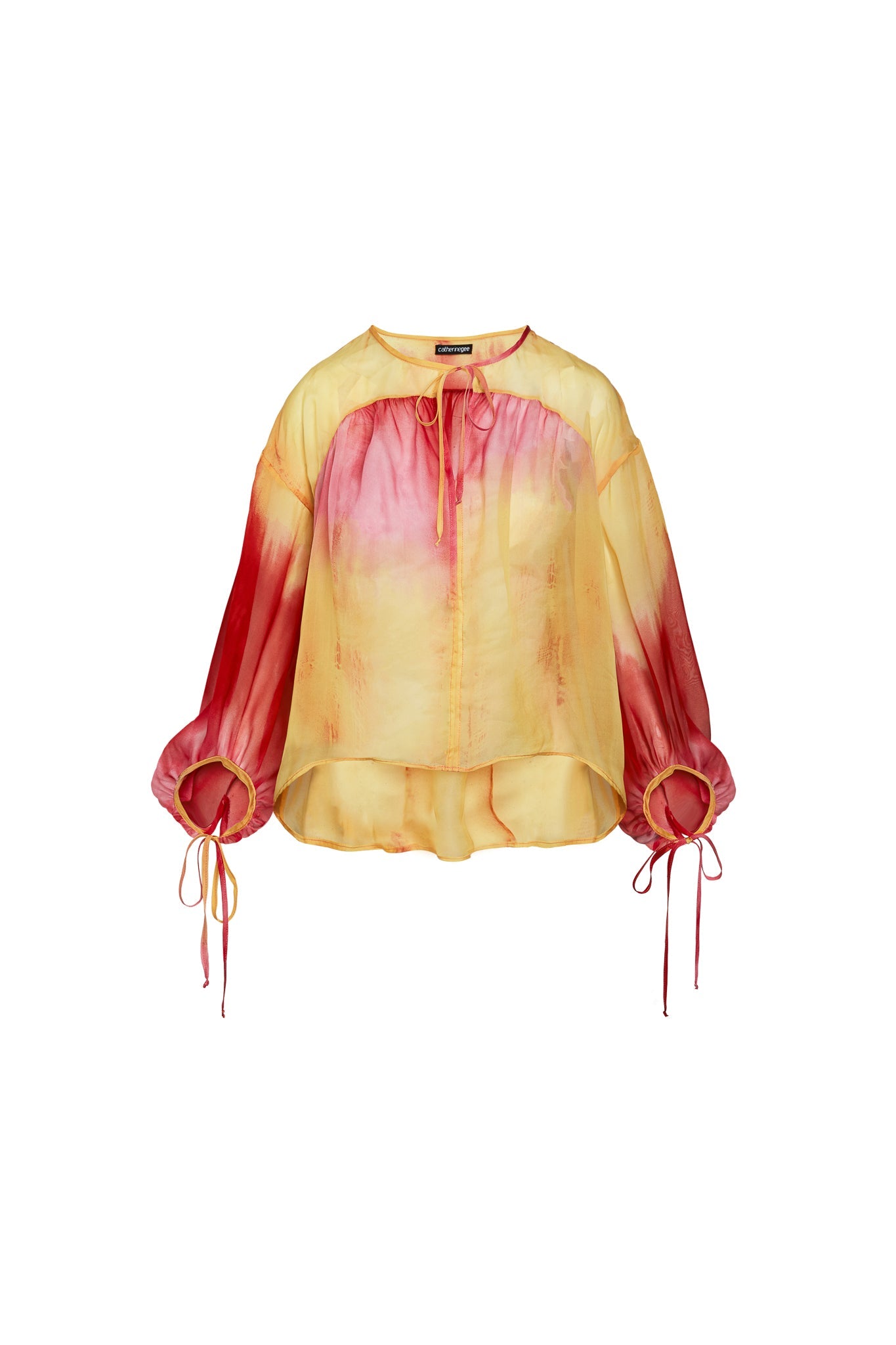 Catherine Gee Frances Santa Barbara Sunset blouse features a vibrant gradient design with shades of yellow and red, reminiscent of a sunset. It has a loose, flowy fit with long sleeves that gather at the wrists, tied with drawstrings. The neckline is round with a small keyhole opening, also tied with a drawstring. The hem is slightly asymmetrical, being longer at the back. The fabric appears lightweight and semi-sheer, adding to its airy and elegant look.