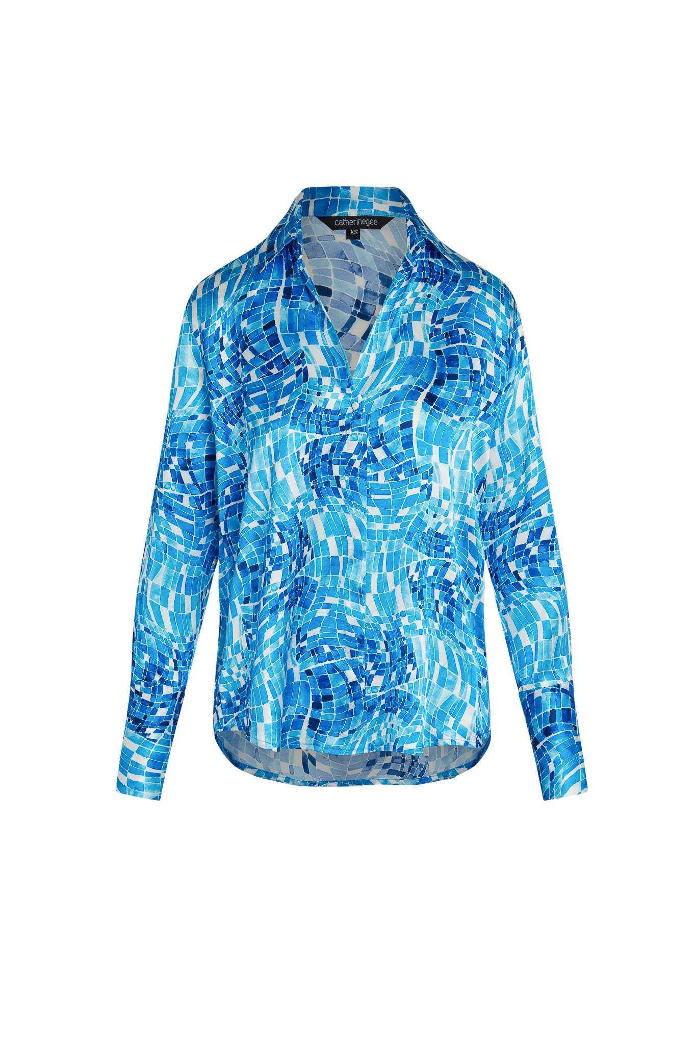 Catherine Gee Daria French Cuff Silk Pool Mosaic Blouse features a vibrant mosaic pattern in various shades of blue and white, resembling a pool or water theme. The blouse has a V-neckline and long sleeves with French cuffs and appears to be lightweight and silky, giving it a luxurious and elegant look.