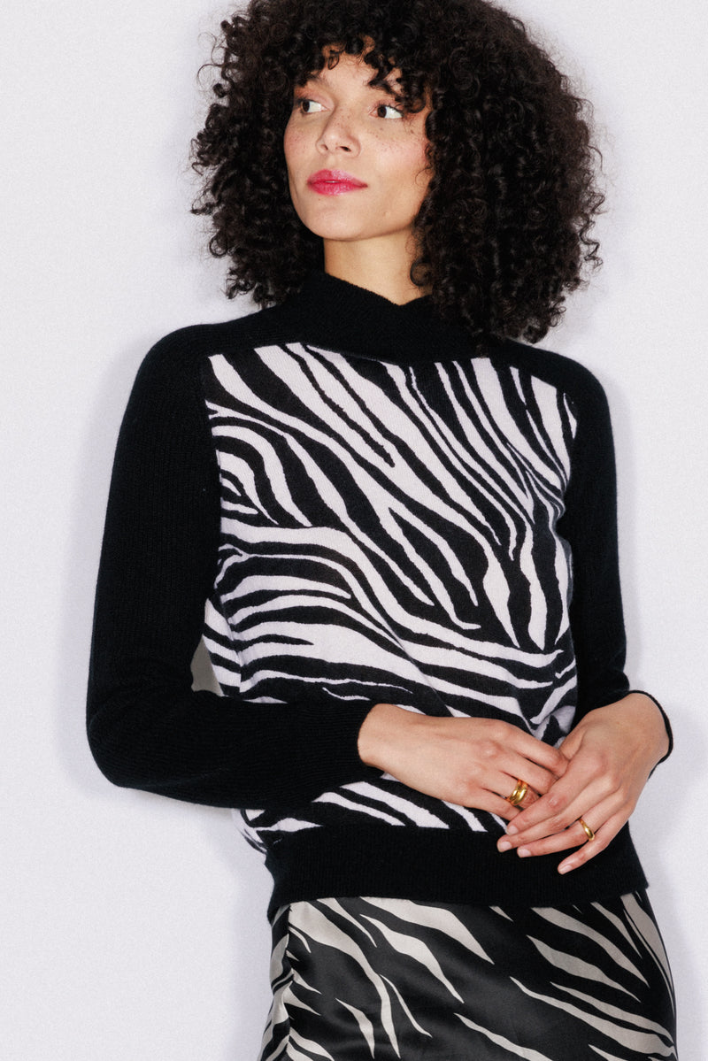 A woman wearing the Catherine Gee Gwen Color Block Cashmere Zebra Sweater. This luxurious sweater features a striking zebra print pattern on the front, combining black and white hues for a bold look. The sleeves and back are solid black, offering a chic contrast. Made from high-quality cashmere, this sweater is both comfortable and stylish making overall design makes it a standout piece for any wardrobe.