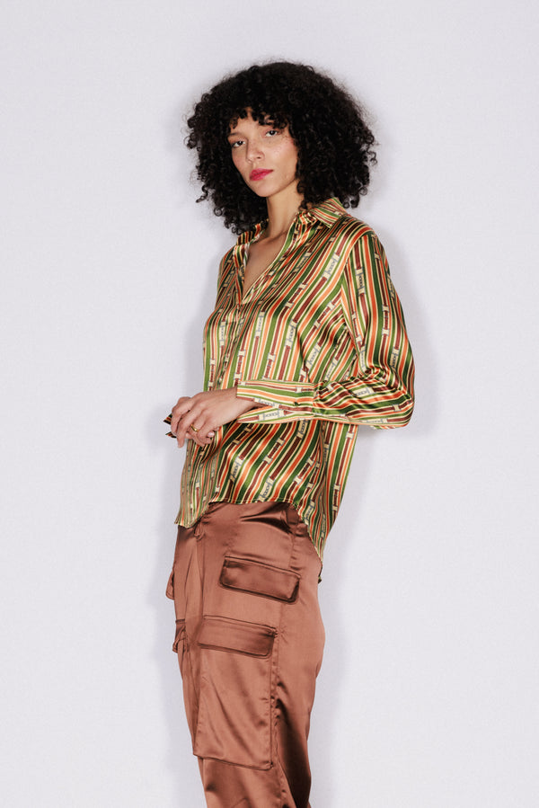 A woman wearing a Catherine Gee Daria French Cuff Silk Thin Belt blouse features a vibrant, multi-colored striped pattern with a silky texture paired with brown cargo pants with multiple pockets. The blouse has a classic collar and long sleeves with French cuffs, giving it a sophisticated and stylish look. The combination of the blouse and pants creates a fashionable and modern outfit.