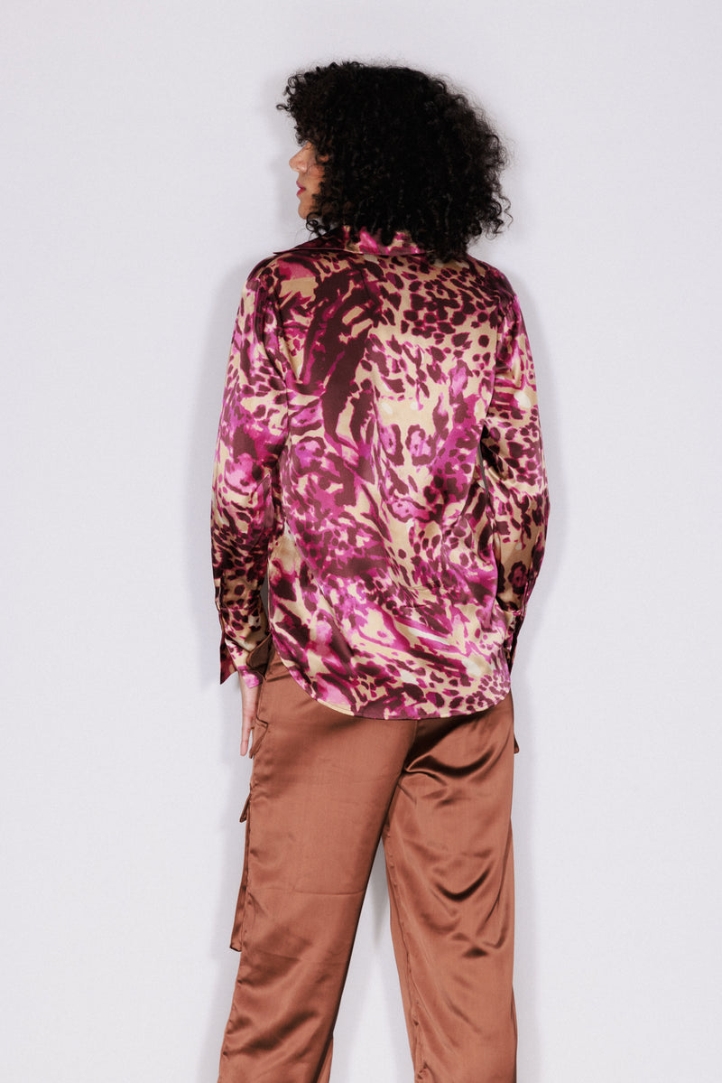 A woman shown from the back wearing a Catherine Gee Daria French Cuff Silk Fuchsia Feline blouse features a vibrant pattern with shades of pink and beige, resembling an animal print paired with brown pants.