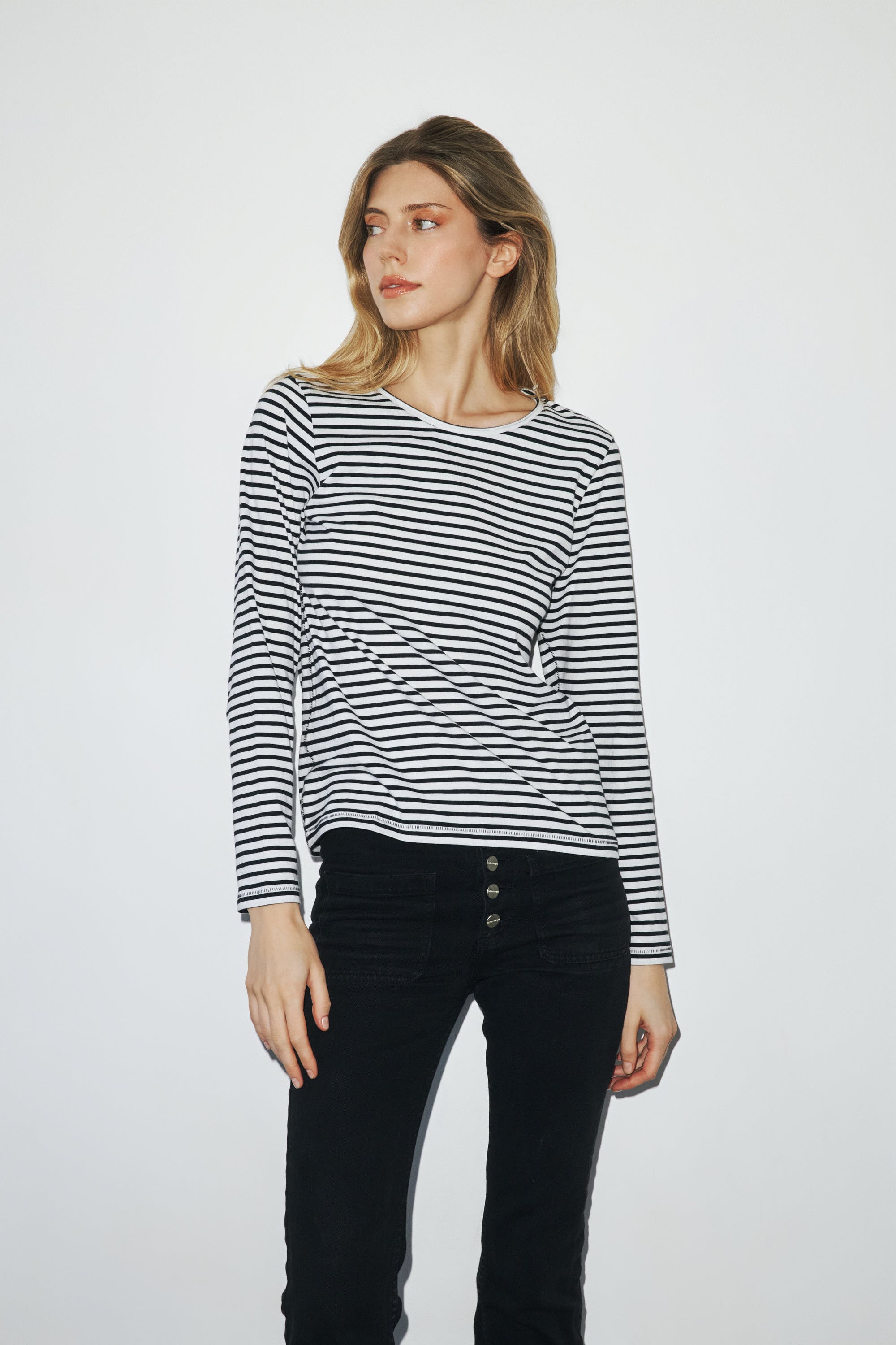 Woman wearing a black and white striped long-sleeve T-shirt by Catherine Gee with a round neckline, paired with high-waisted black pants with three visible buttons.