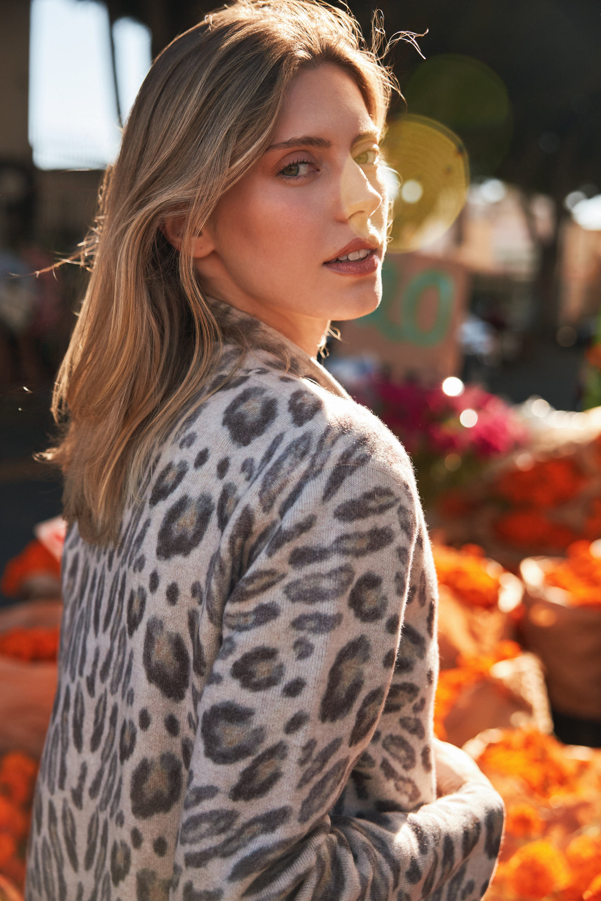 A woman stands against a vibrant backdrop of flowers wearing a Catherine Gee Double Face Cashmere Reversible New Leopard Coat. This luxurious coat features a chic leopard print in grey and black, showcasing its reversible design. The coat's high-quality cashmere fabric and stylish pattern make it a standout piece, perfect for adding elegance and warmth to any outfit.