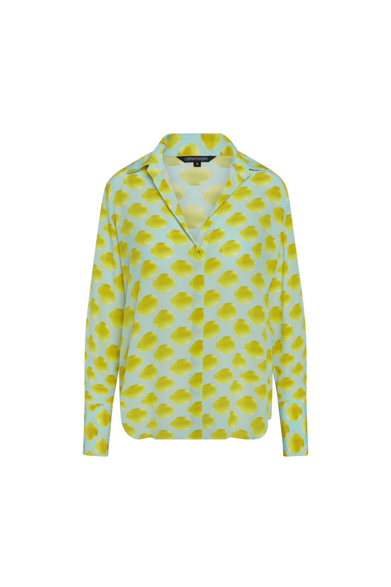 Catherine Gee Daria French Cuff Silk Limon Blue blouse features a light blue background with a pattern of yellow lemon-like spots. It has a V-neck with a collar and long sleeves with French cuffs. The fabric appears to be smooth and silky, giving it a luxurious look.