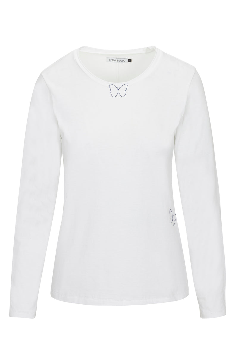 Catherine Gee Embroidered Cotton Long Sleeve Butterfly T-Shirt. The shirt is white in color with a simple, elegant design featuring two small embroidered butterfly outlines, one located near the neckline and the other near the lower right side. It has a round neckline and long sleeves, making it suitable for cooler weather and the minimalist butterfly embroidery adds a delicate and feminine touch to the overall design.