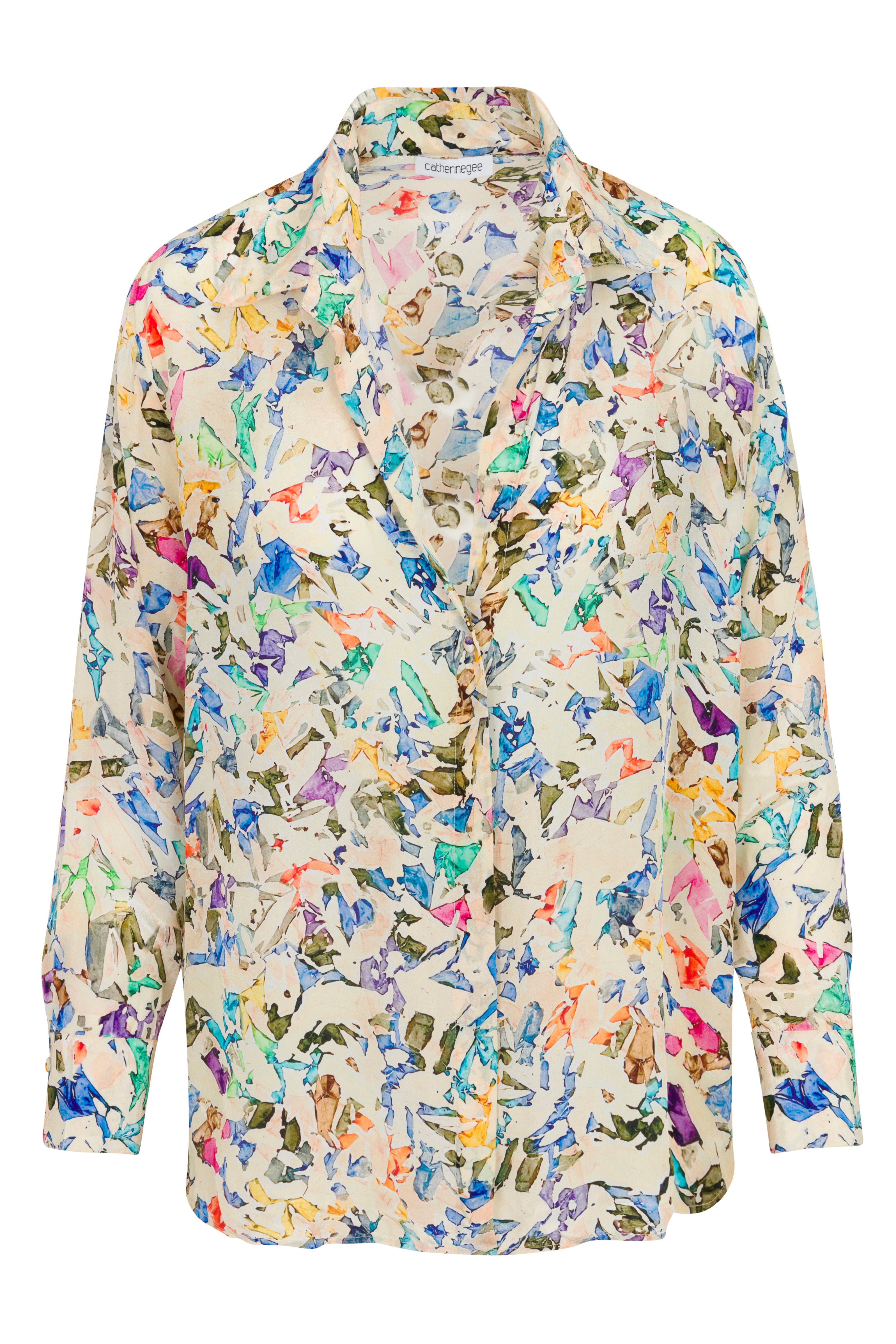 A Catherine Gee Dakota Blouse - Museo. The blouse features a vibrant, abstract print with a mix of colors including blue, green, yellow, orange, and purple on a light beige background. It has a relaxed fit with long sleeves and a button-down front. The fabric appears lightweight and flowy, suitable for a casual or semi-formal look.