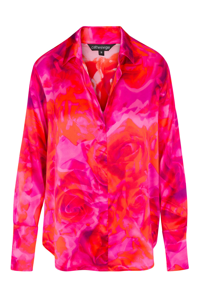 A vibrant Catherine Gee Daria French Cuff Silk-Hot Roses blouse in the Hot Roses pattern features a bold and colorful design with shades of red, pink, and orange hues, resembling abstract roses. It has a classic collar, long sleeves with French cuffs, and a button-down front.