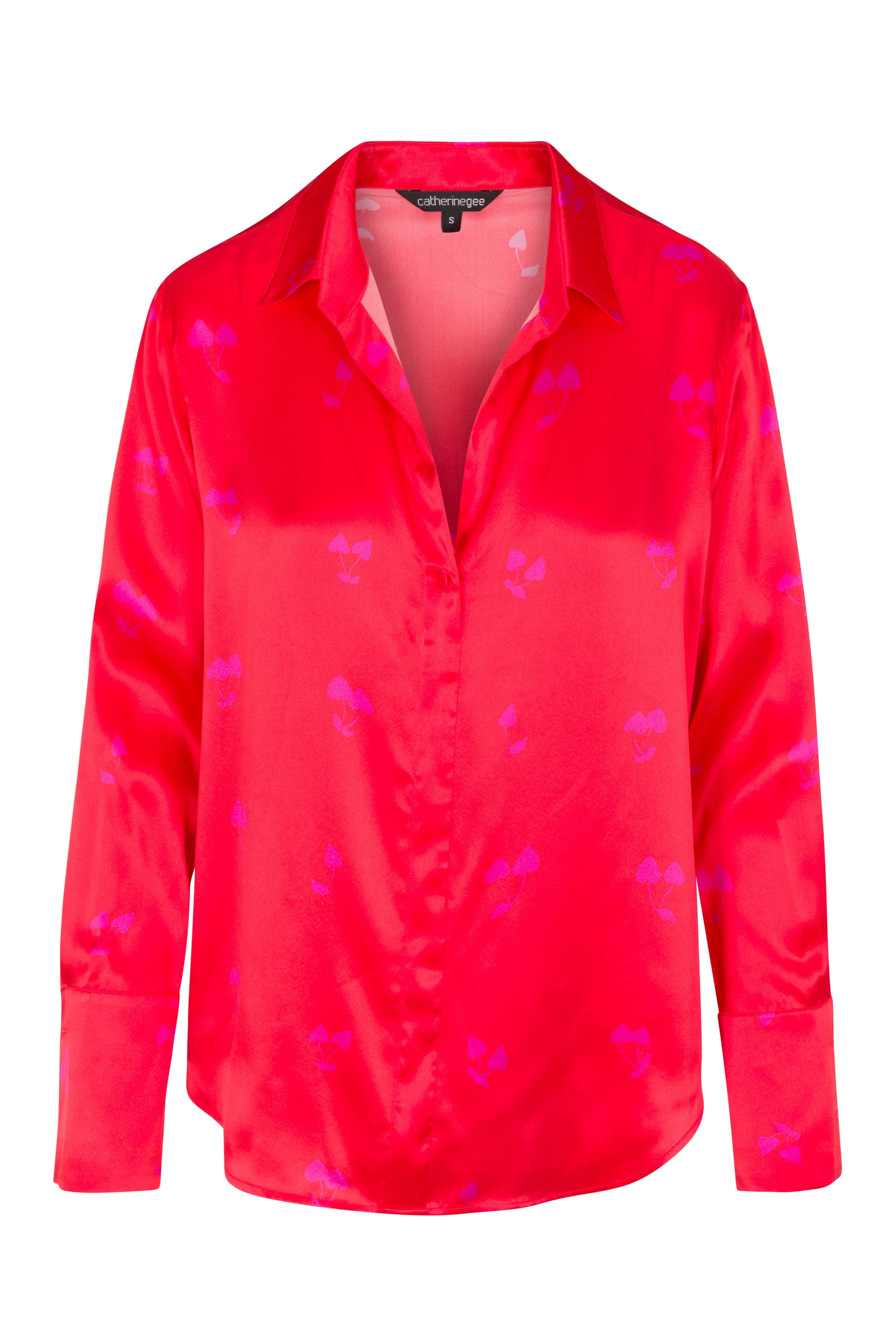 Catherine Gee Daria French Cuff Silk-Cherry Heart blouse is a vibrant red color with a subtle heart pattern in a slightly darker shade. It features a classic collar, a deep V-neckline, and long sleeves with French cuffs.