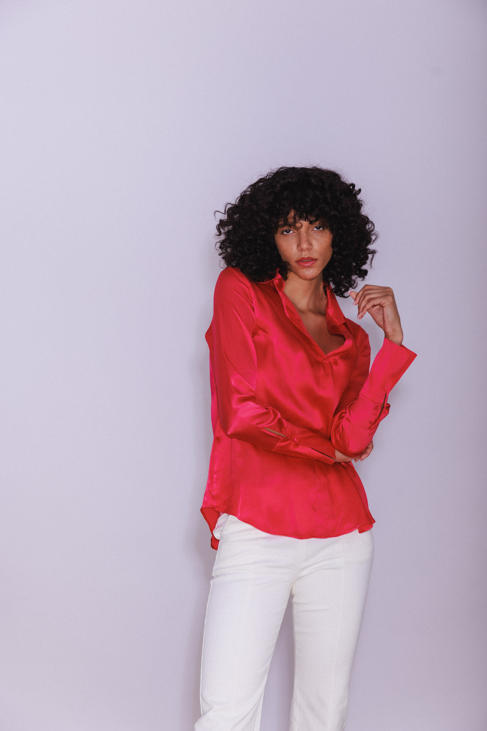 A woman wearing a Catherine Gee Daria French Cuff Silk Blouse - Electric Pink. A vibrant electric pink silk blouse with French cuffs, paired with white pants. The blouse has a shiny, smooth texture and a relaxed fit, with the person posing against a plain light-colored background.
