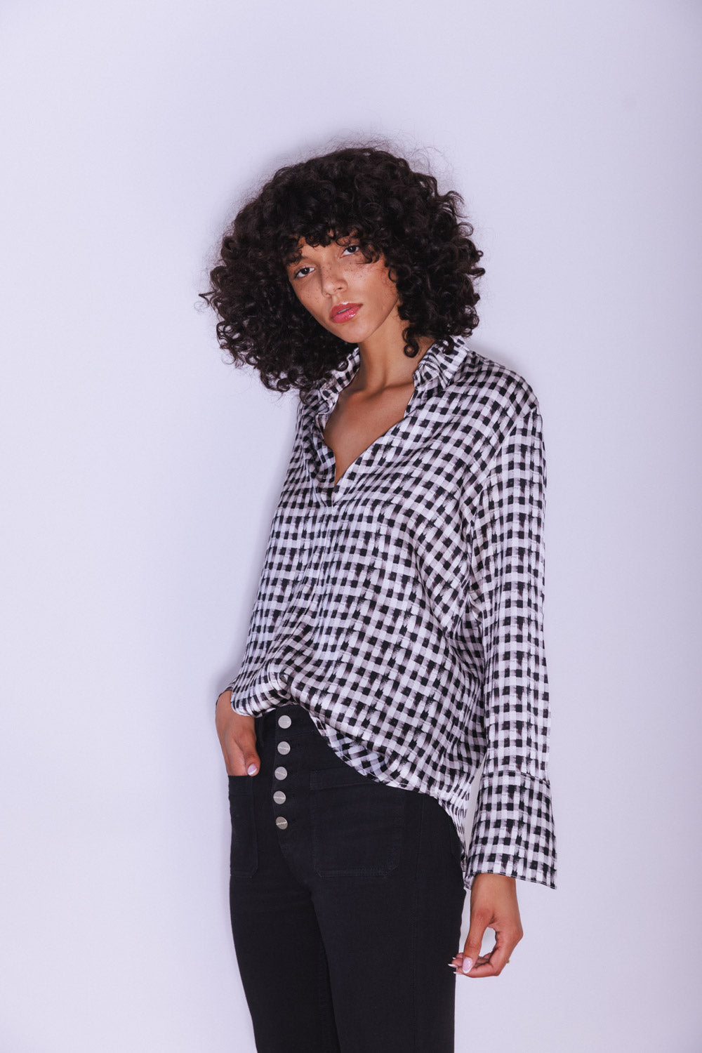 Woman wearing a Catherine Gee Daria French Cuff Silk-Grosgrain Black and White blouse featuring a black and white checkered pattern, French cuffs, and black pants with buttons on a plain white background.