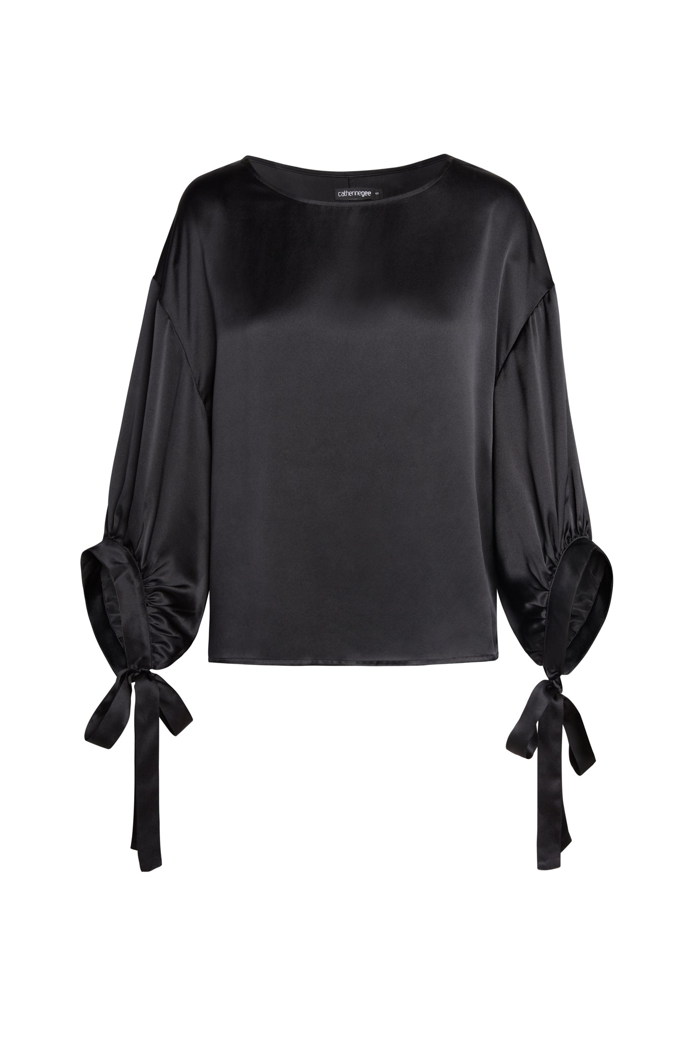 A black Catherine Gee Constance Blouse satin blouse with long, loose sleeves that gather at the wrists with ribbon ties. The blouse has a simple, elegant design with a round neckline and a relaxed fit. The fabric has a smooth, shiny finish, giving it a luxurious appearance.