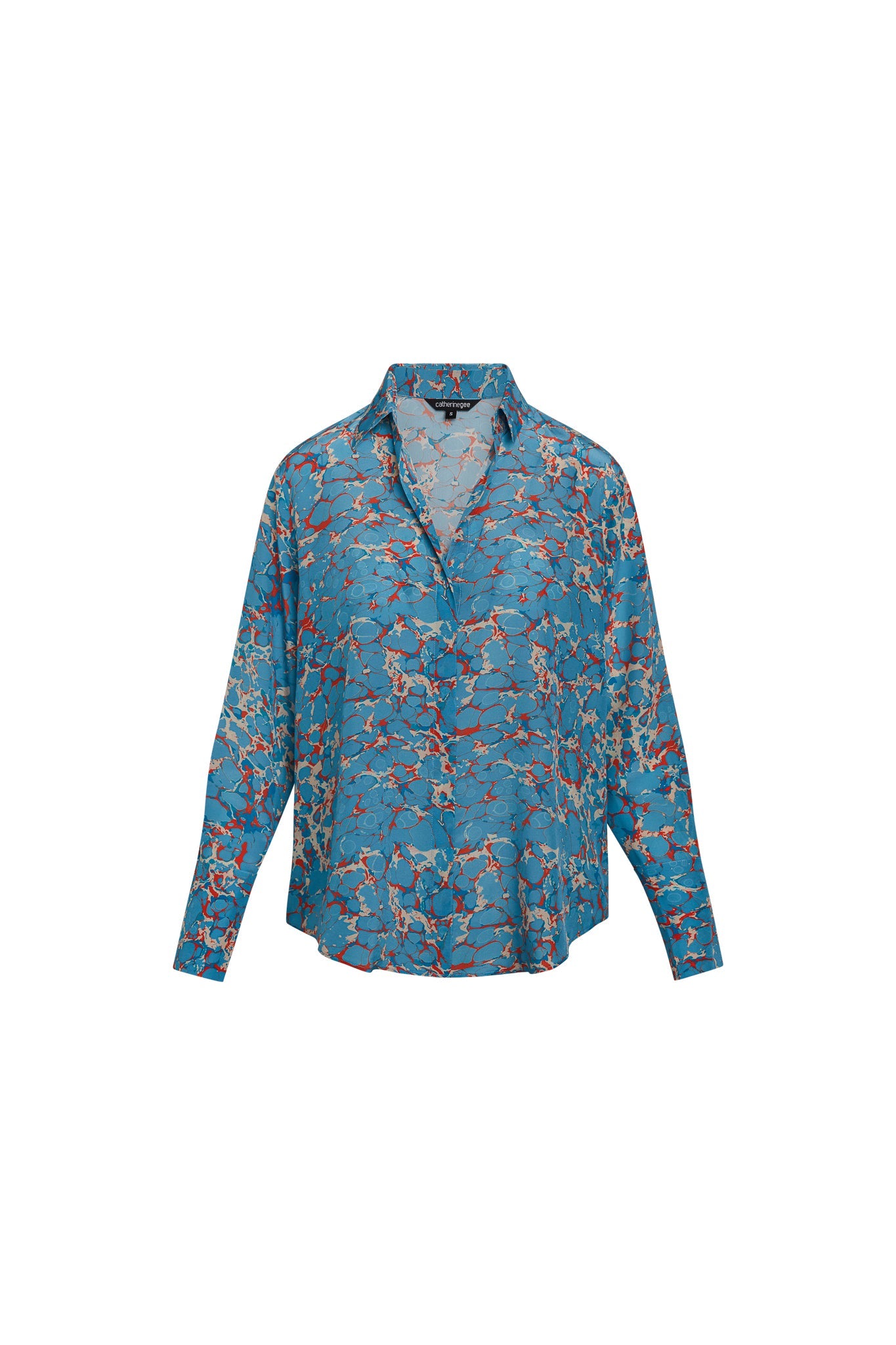 Catherine Gee Daria French Cuff Silk Blouse Corfu. A blue silk blouse with a vibrant, abstract pattern featuring shades of red, white, and beige. The blouse has a relaxed fit with long sleeves and a collar.