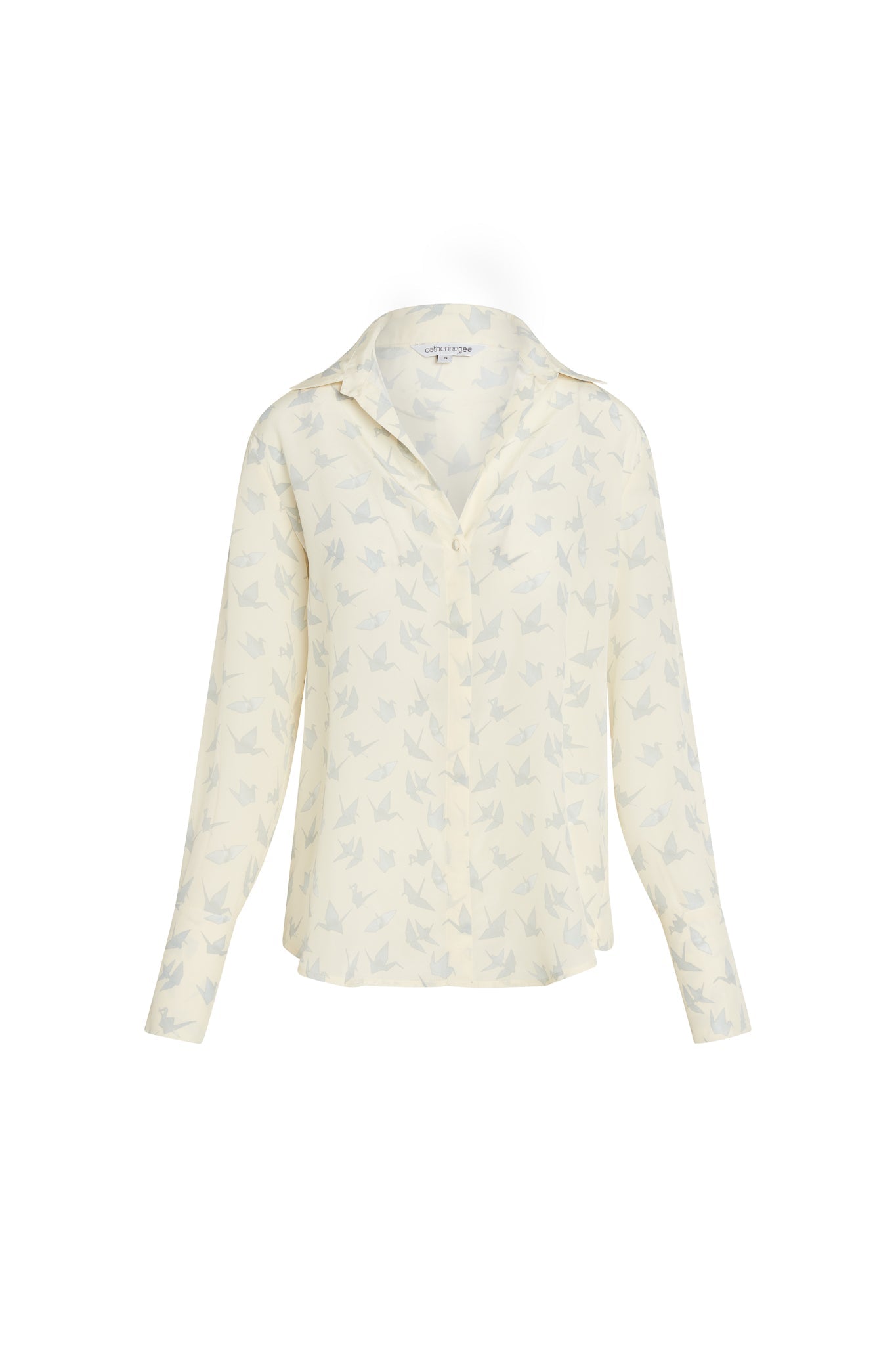 A Catherine Gee Daria French Cuff Silk Neutral Crane blouse features a silk and a neutral color with a delicate crane pattern. It has long sleeves with French cuffs and a classic collar. The fabric appears lightweight and elegant, making it suitable for both casual and formal occasions. The crane pattern adds a unique and refined touch to the overall design.
