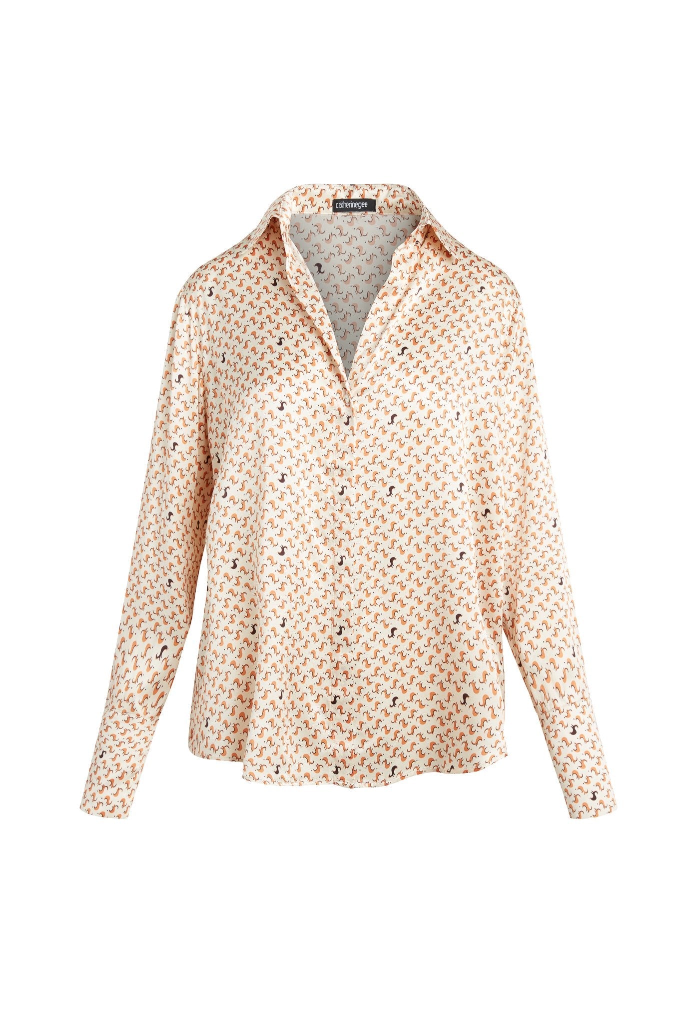 A Catherine Catherine Gee Daria French Cuff Silk-Lexi Print blouse features a light cream background with a small, repetitive pattern in shades of orange and blue accents. It has a classic collar, long sleeves, and a relaxed fit. The fabric appears smooth and slightly shiny.