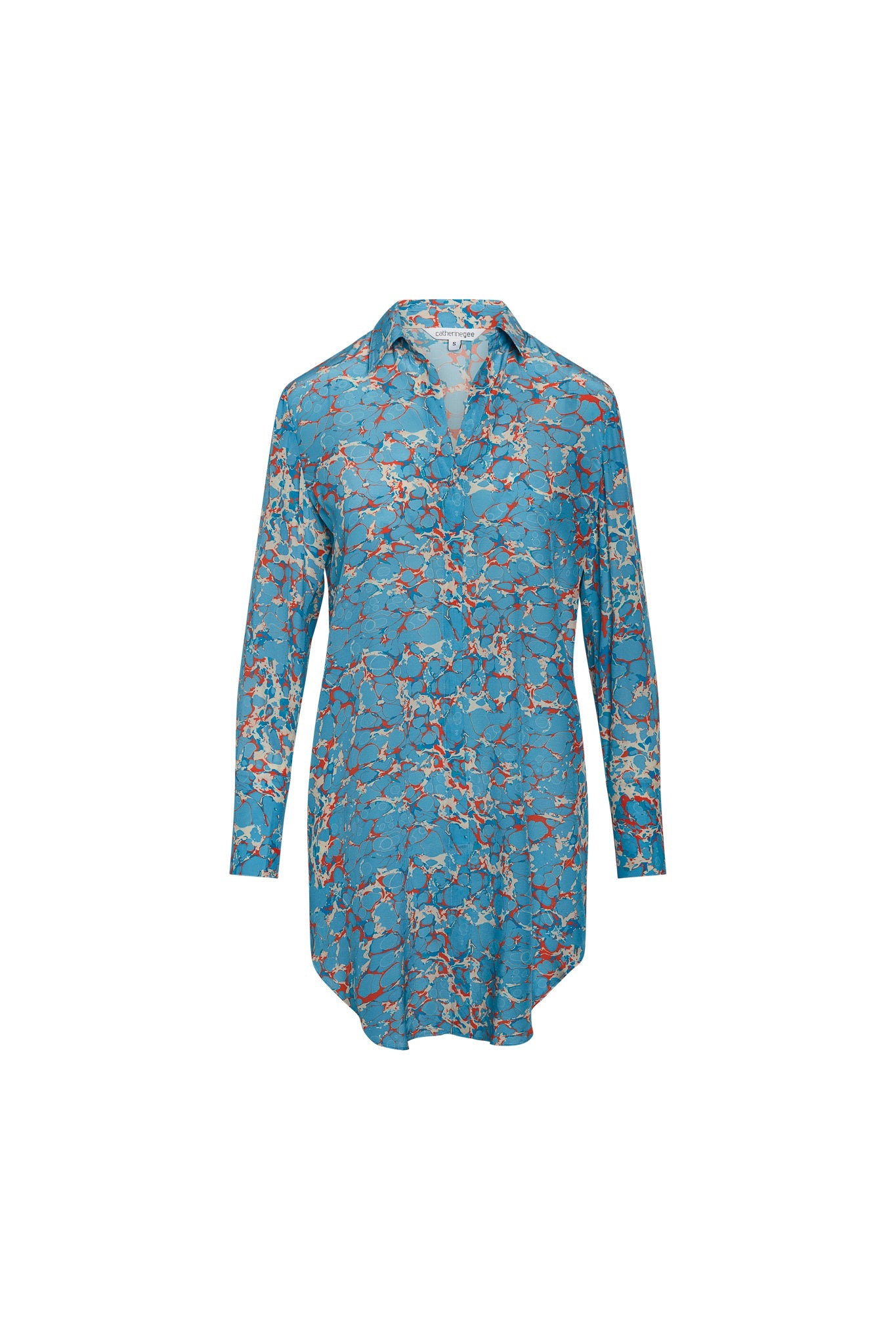 Catherine Gee Daria Silk Shirt Corfu Dress. This elegant dress features a vibrant blue base color with intricate red and white patterns. The shirt-style dress has a collared neckline, long sleeves, and a curved hemline that falls above the knee. Made from luxurious silk, the dress offers a sophisticated and stylish look suitable for both casual and semi-formal occasions. The intricate design and quality material make it a standout piece.