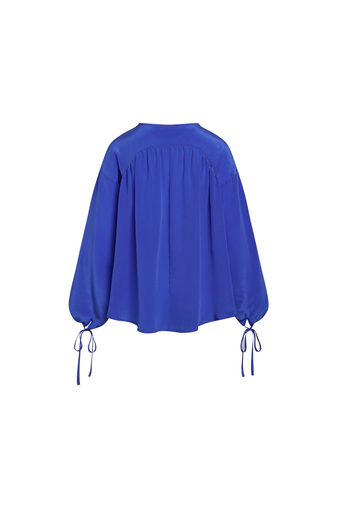 Back-view of a Catherine Gee Frances French Blue Blouse. The blouse is a vibrant blue color with a loose, flowing fit and features long, voluminous sleeves that gather at the wrists with adjustable ties. The back has a yoke with subtle gathers, adding to the blouse's elegant and relaxed silhouette. The fabric appears to be lightweight and silky, contributing to its sophisticated and stylish appearance.