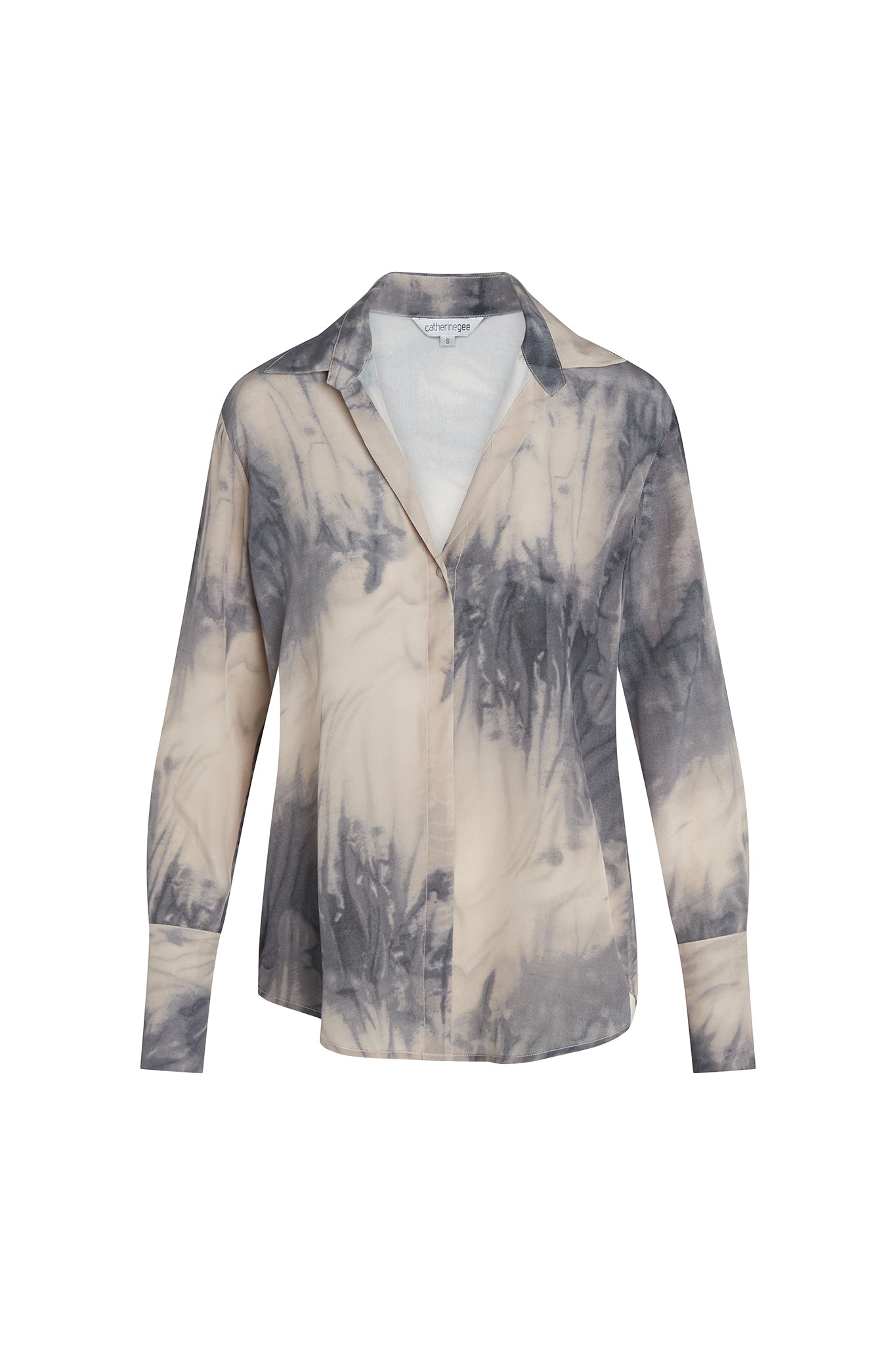 Catherine Gee Daria French Cuff Silk Smoke blouse features a tie-dye pattern in shades of gray and white, creating a smoky effect. It has a classic collar, long sleeves with French cuffs, and a button-down front. The silk material gives it a luxurious and elegant appearance, making it suitable for both casual and formal occasions.